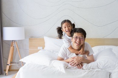 happy asian family father and daughter relaxing and smiling on white bed