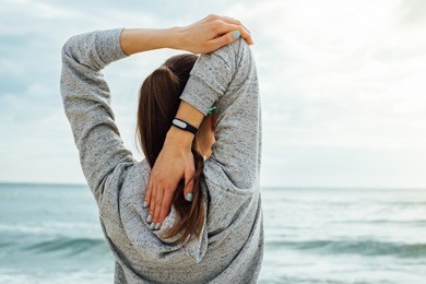 girl in sportswear stretches the triceps in the early morning on the beach. view from the back.
