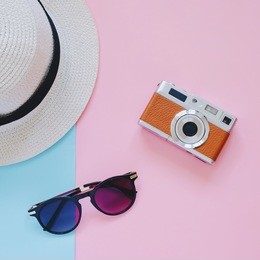 creative flat lay fashion style with camera, sunglasses and panama hat on pastel color background