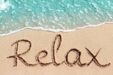 word relax handwritten on sandy beach