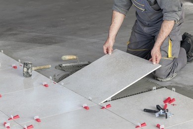 ceramic tiles. tiler placing ceramic wall tile in position over adhesive with lash tile leveling system