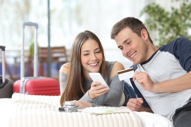 couple of tourists ready for travel booking hotel on line with credit card and mobile phone on the bed 
