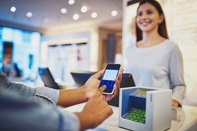 close up view on fingers of customer entering information on phone in front of register as female cashier smiles in store
