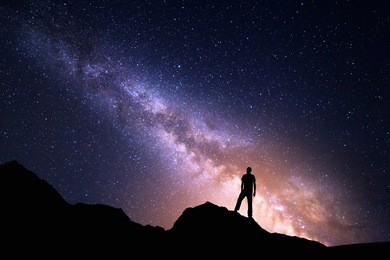 landscape with milky way. night sky with stars and silhouette of a happy man on the rock. beautiful universe. space background