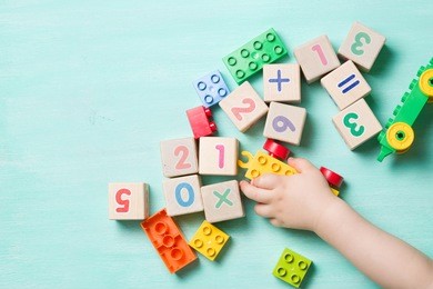 child playing with wooden cubes with numbers and colorful toy bricks on a turquoise wooden background. toddler learning numbers. hand of a child taking toys.