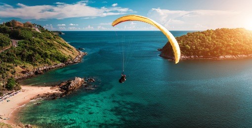 skydiver flying over the water during sunset with the mountains