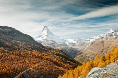 view on autumn forest, snowy matterhorn, mountains and blue sky with white clouds, switzerland 