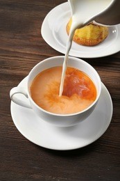 milk poured into a cup of tea on wooden background.
