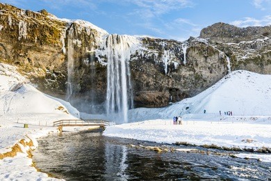 frozen beautiful waterfall seljalandsfoss under the sunrise lights in winter, reflection in river. iceland.
