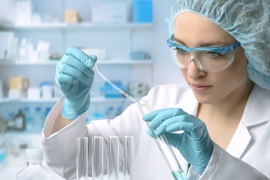young female tech or scientist loads liquid sample into test tube with plastic pipette. shallow dof, focus on the hand with the tube.