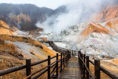 jigokudani hell valley walking trail in noboribetsu, hokkaido, japan. selective focus at front banister of wooden footpath.