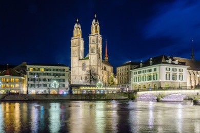 view of the grossmunster (great minster) church and the limmat river at night, with a christmas tree, in zurich, switzerland