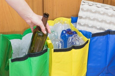 female hand is sorting empty wine bottle to the green bag. household waste concept.