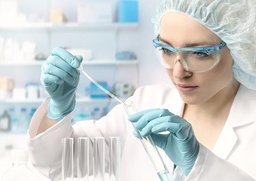 young female tech or scientist loads liquid sample into test tube with plastic pipette. shallow dof, focus on the hand with the tube.