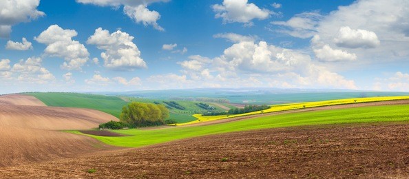 big panoramic view of beautiful spring hills landscape with colorful fields, sunny day sky