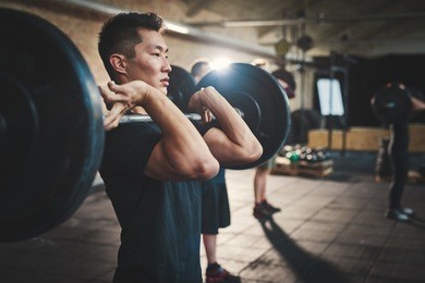 fit young man lifting barbells looking focused, working out in a gym with other people