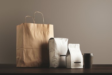 presentation of retailer package set: craft paper bag, big pouch, small container and take away glass with cap. filled with goods, blank labeled, merchandise pack