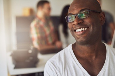 close up of handsome smiling worker in white shirt and eyeglasses with three out of focus employees behind him in meeting