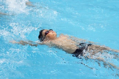 healthy boy back stroke swims in swimming pool , asian young kid training with swim goggles 