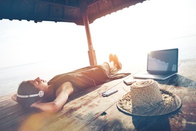 resting woman with laptop listening music with headphones in shadow shelter. blurry effect, lens flares effect, vintage color