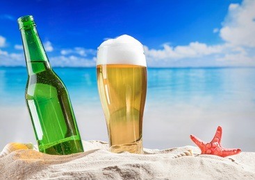 bottle of beer with full glass in sand at beach.