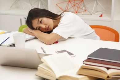 tired asian student resting after hard-working day in library. exhausted woman lying on table with her eyes opened.