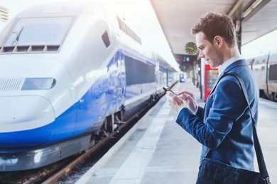 man using mobile application on his smartphone at train station, business travel