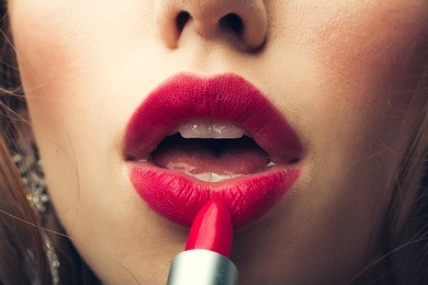 young woman doing makeup with lipstick on open mouth closeup