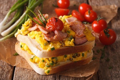double sandwich with scrambled eggs, bacon and tomatoes close-up on the table. horizontal