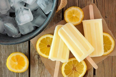 homemade lemon yogurt popsicles with fresh lemon slices on paper with rustic wood background