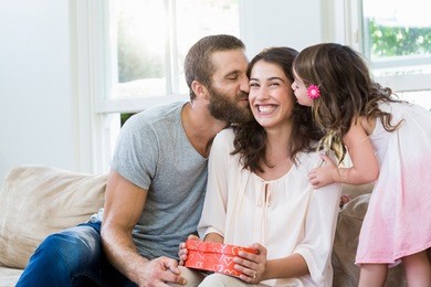 happy mother receiving a gift from her husband and daughter in living room