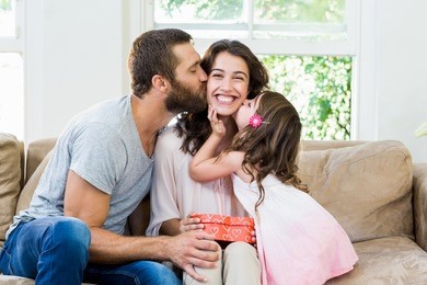 happy mother receiving a gift from her husband and daughter in living room