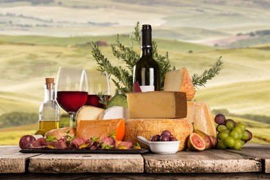 delicious cheeses with red wine on wooden table. italian countryside, tuscany.
