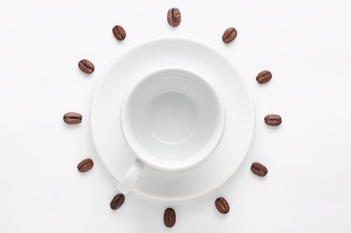 empty coffee cup on saucer and coffee beans against white background forming clock dial viewed from above. concept is time to drink morning coffee.