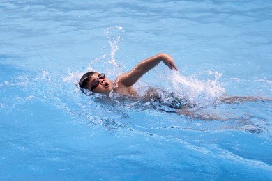 healthy boy front crawl swims in swimming pool , asian young kid training with swim goggles