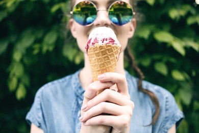 outdoor closeup fashion portrait of young hipster crazy girl eating ice cream in summer hot weather in round mirror sunglasses have fun and good mood. toned style instagram filters