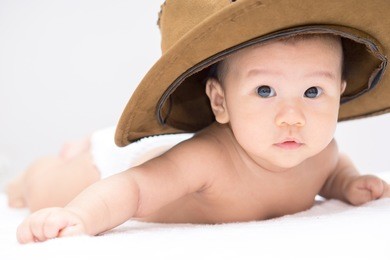 asian baby with cowboy hat lying on stomach and raising his head