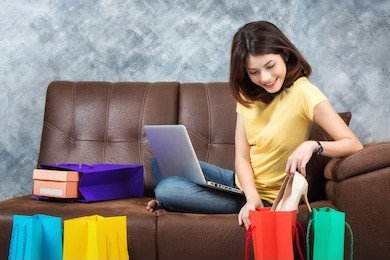 young beautiful asian woman sitting on sofa shopping online with shopping bags at home.