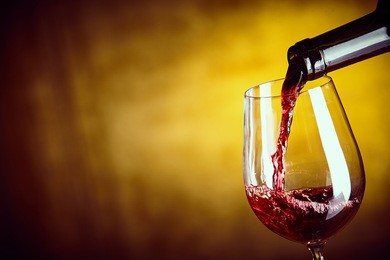 serving a glass of red wine from a bottle with a close up view of the wine being poured into the bowl of an elegant wine glass over an abstract yellow brown background with copy space