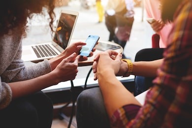 closeup of woman is reading text message on mobile phone in network, while is sitting with laptop computer in co-working cafe. group of friends are using gadgets during recreation time in coffee shop 