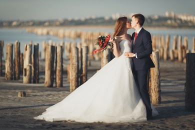 wedding couple, groom, bride with bouquet posing near sea on sunset