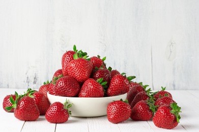 heap of fresh strawberries in ceramic bowl on rustic white wooden background. 
