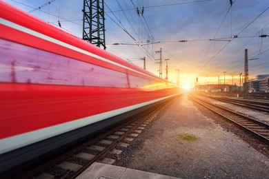 high speed red passenger train on railroad track in motion at sunset. blurred commuter train. railway station in nuremberg, germany. industrial landscape