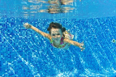 child swims in pool underwater, happy active girl has fun under water, kid sport on family vacation
