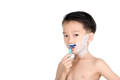 young boy is shaving his face in the bathroom.
