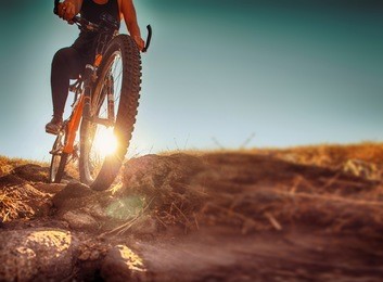 a woman riding a bicycle down a dirt trail with big rocks in the back country to get away from the city toned with a retro vintage instagram filter app or action effect 