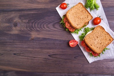 homemade sandwich with egg, salad and tomatoes on crispy slice of rye bread on a dark wooden background. top view with copyspace
