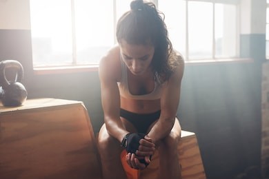 young woman sitting on a box at gym after her workout and looking down. female athlete taking rest after fitness training at gym.