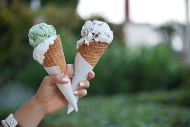 two colorful tasty ice cream cones in hand. (focus on ice cream)