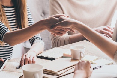 sealing a deal. close-up of two businesswomen shaking hands while sitting at the desk with man in the background 